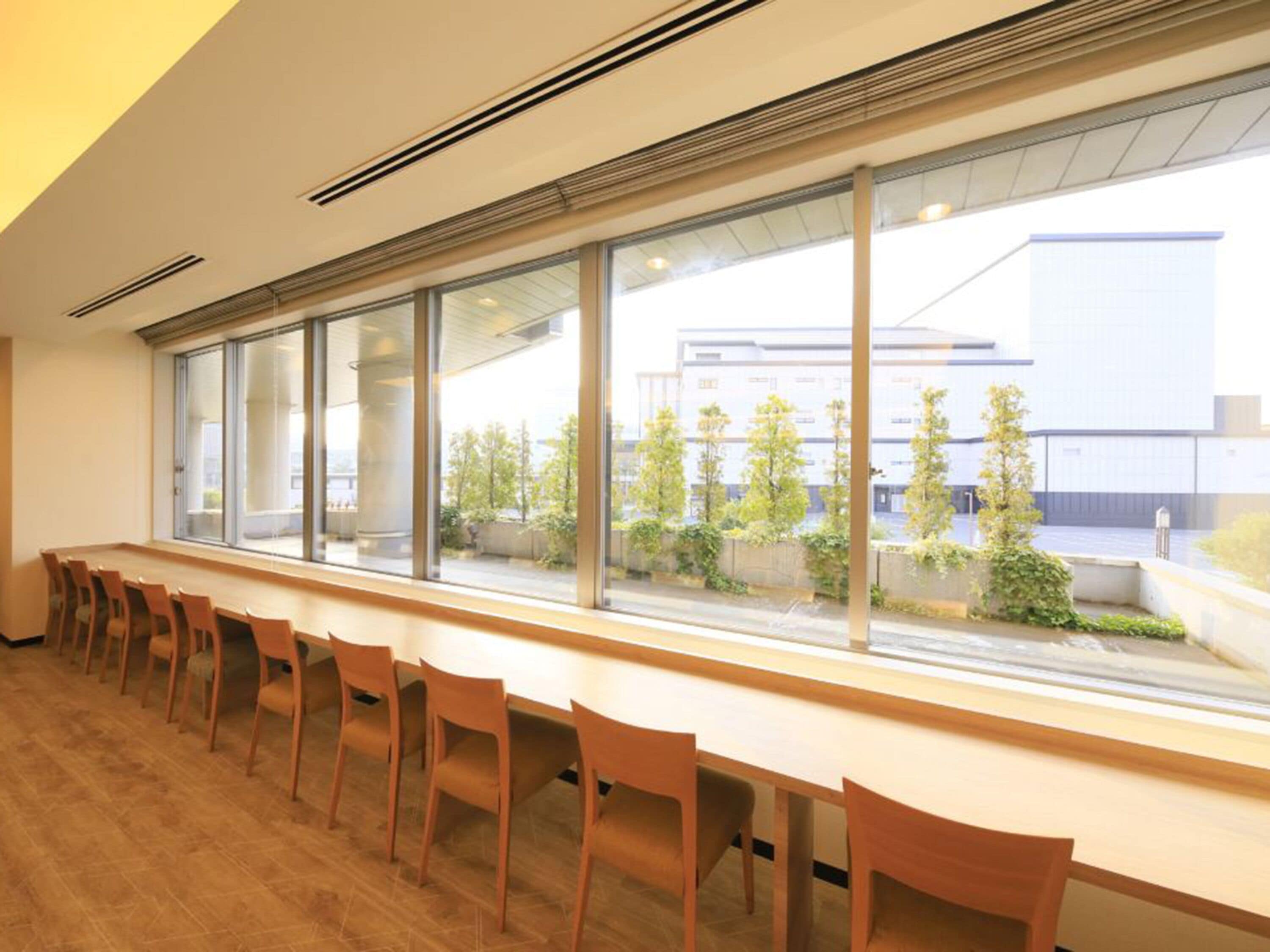 Ein moderner Konferenzraum mit einem langen Tisch und Stühlen, große Fenster mit Blick auf Gebäude und Grünflächen.