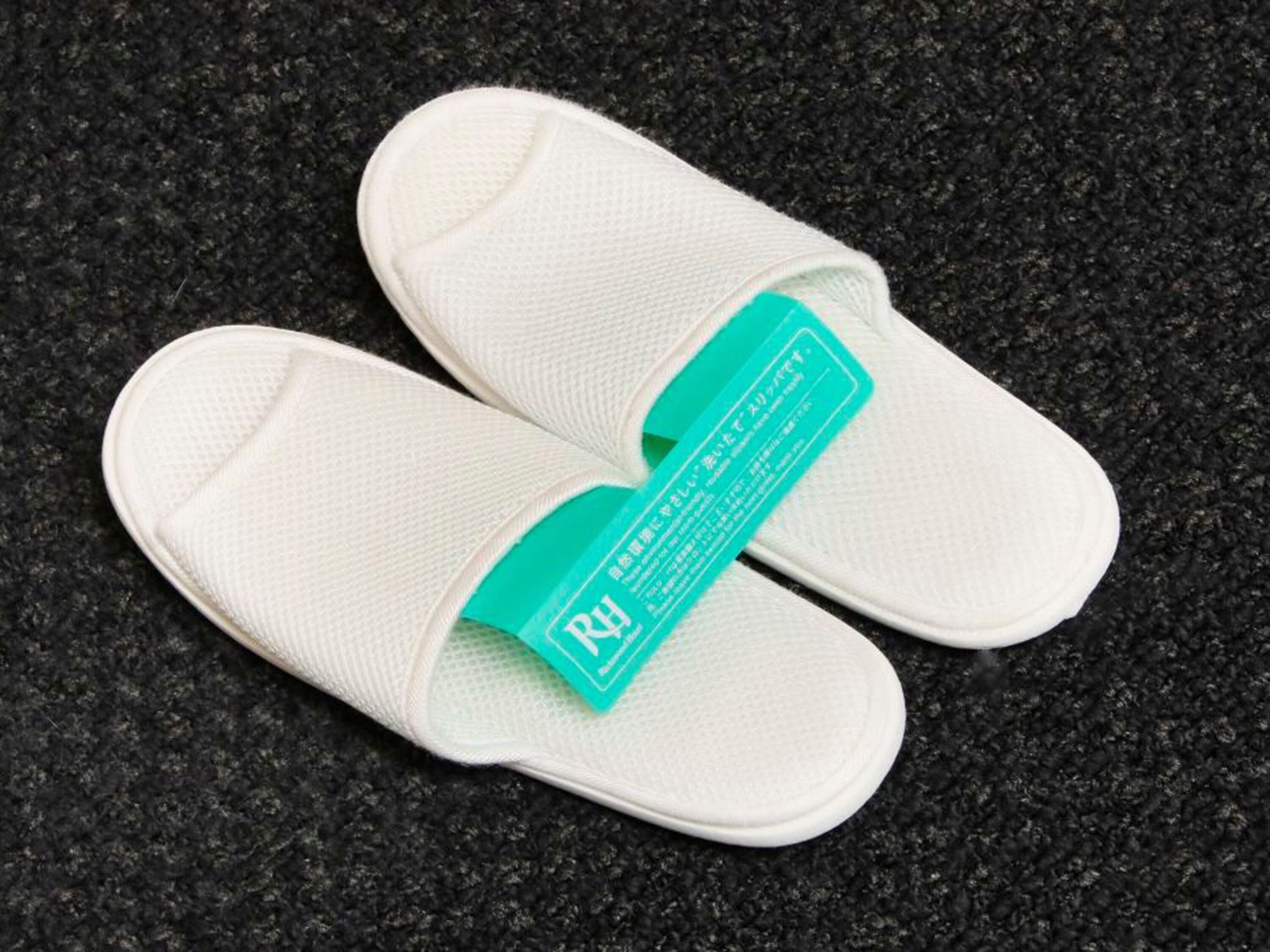 A pair of white slippers with a teal label on a textured surface.
