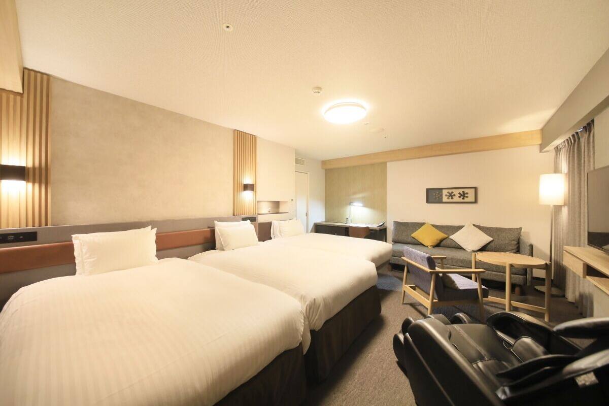 A hotel room with two beds, a sofa, a small table, and a TV.