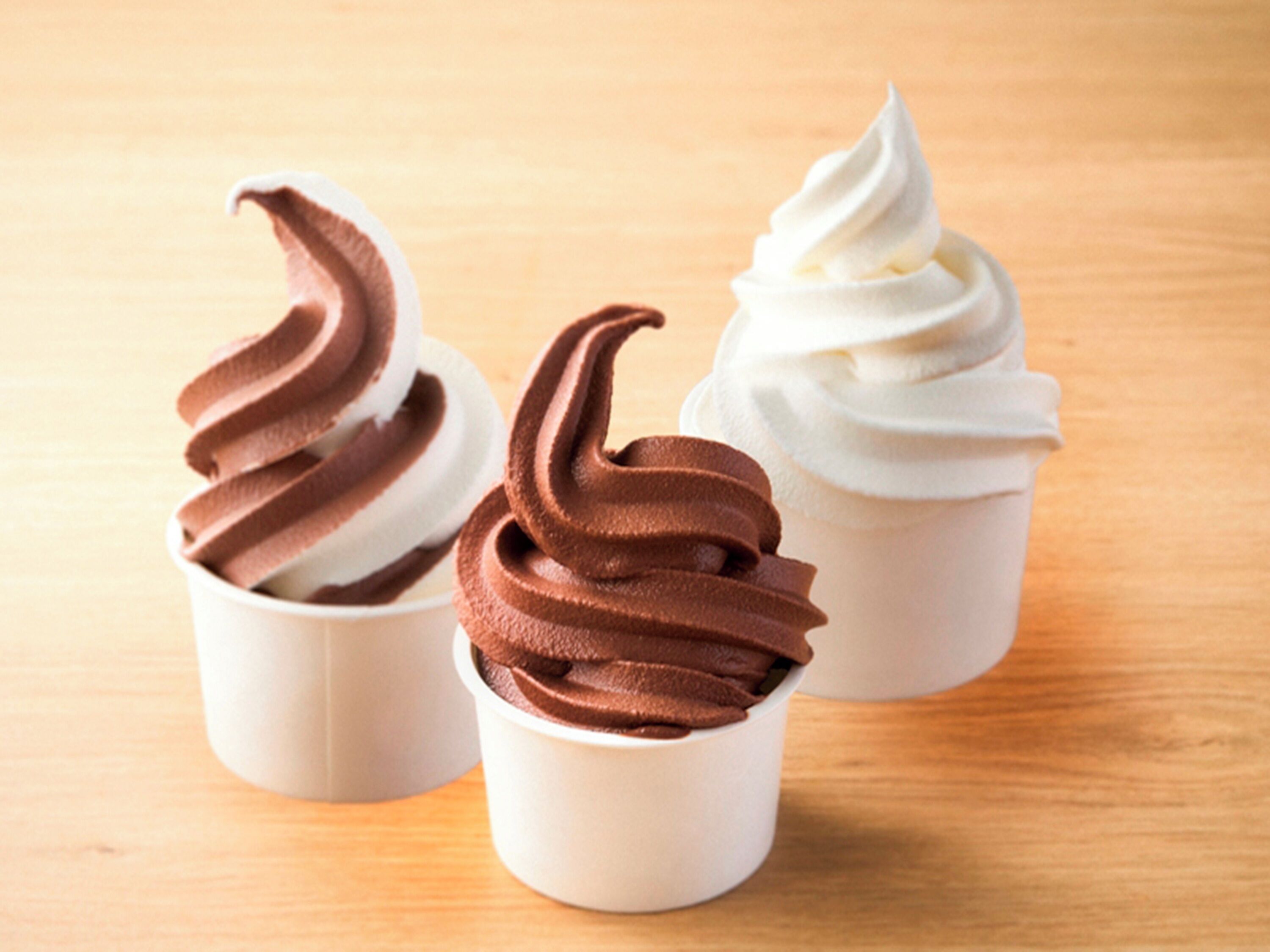 Three cups of ice cream in paper cups on a wooden surface.