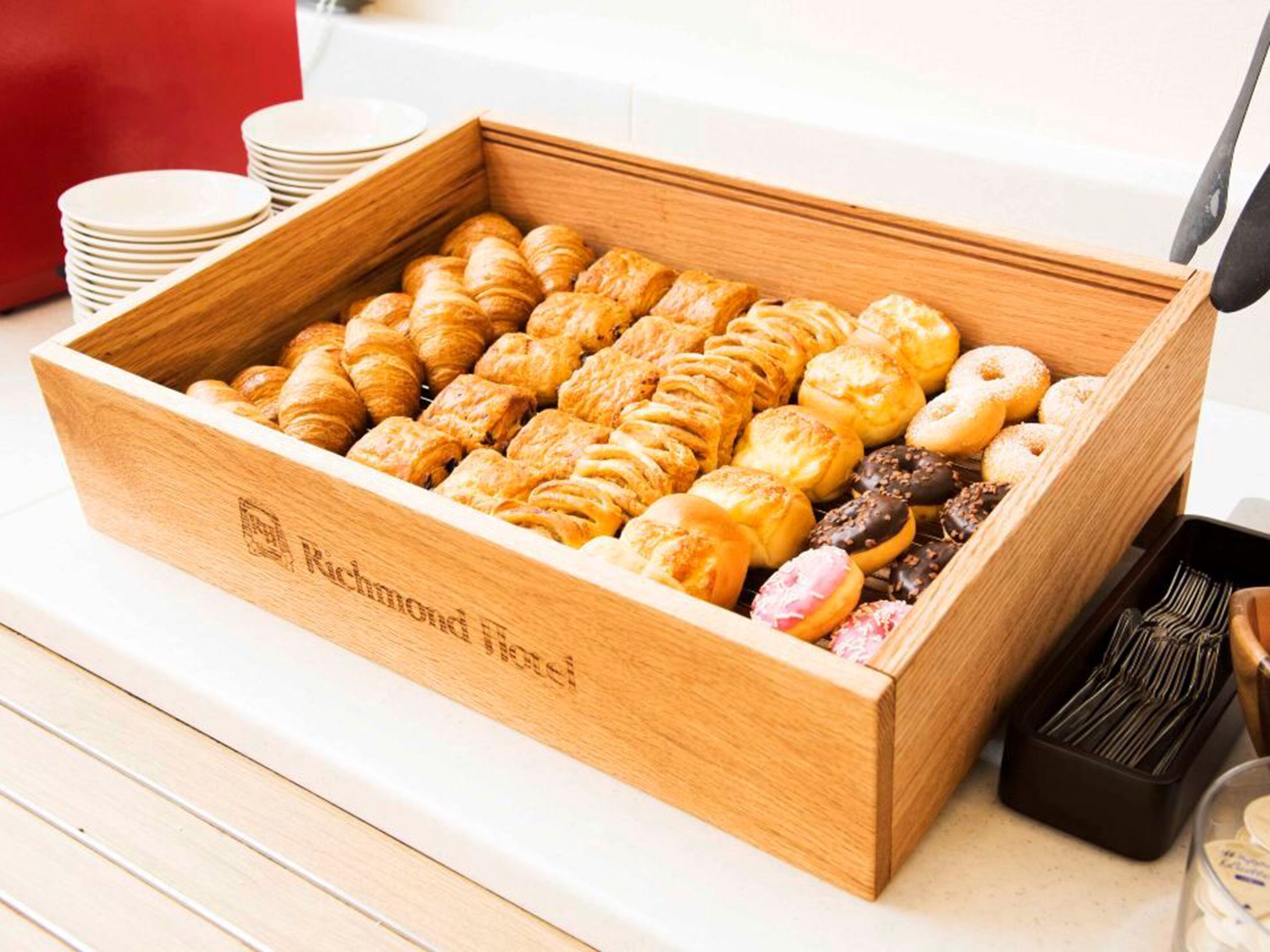 Une boîte en bois remplie de diverses pâtisseries et une pile d’assiettes blanches sur une table.