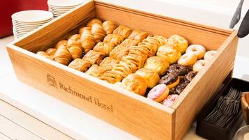 Une boîte en bois remplie de diverses pâtisseries et une pile d’assiettes blanches sur une table.