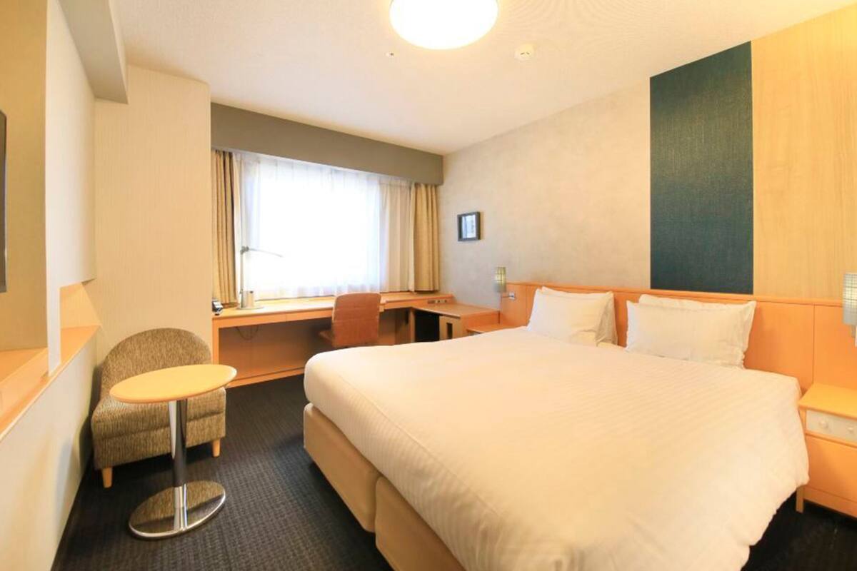 A hotel room with a large bed, a desk, a chair, and a small table.