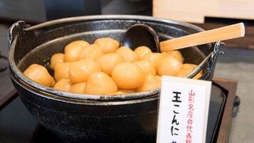 Una pentola nera piena di gnocchi gialli e rotondi, con un cucchiaio di legno all'interno. Accanto alla pentola, un cartello con scritte giapponesi.
