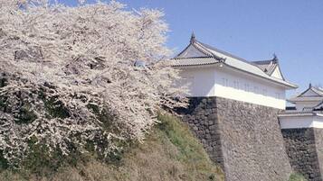 Um castelo japonês tradicional com paredes brancas e base de pedra cinzenta, com vista para um corpo d'água calmo.