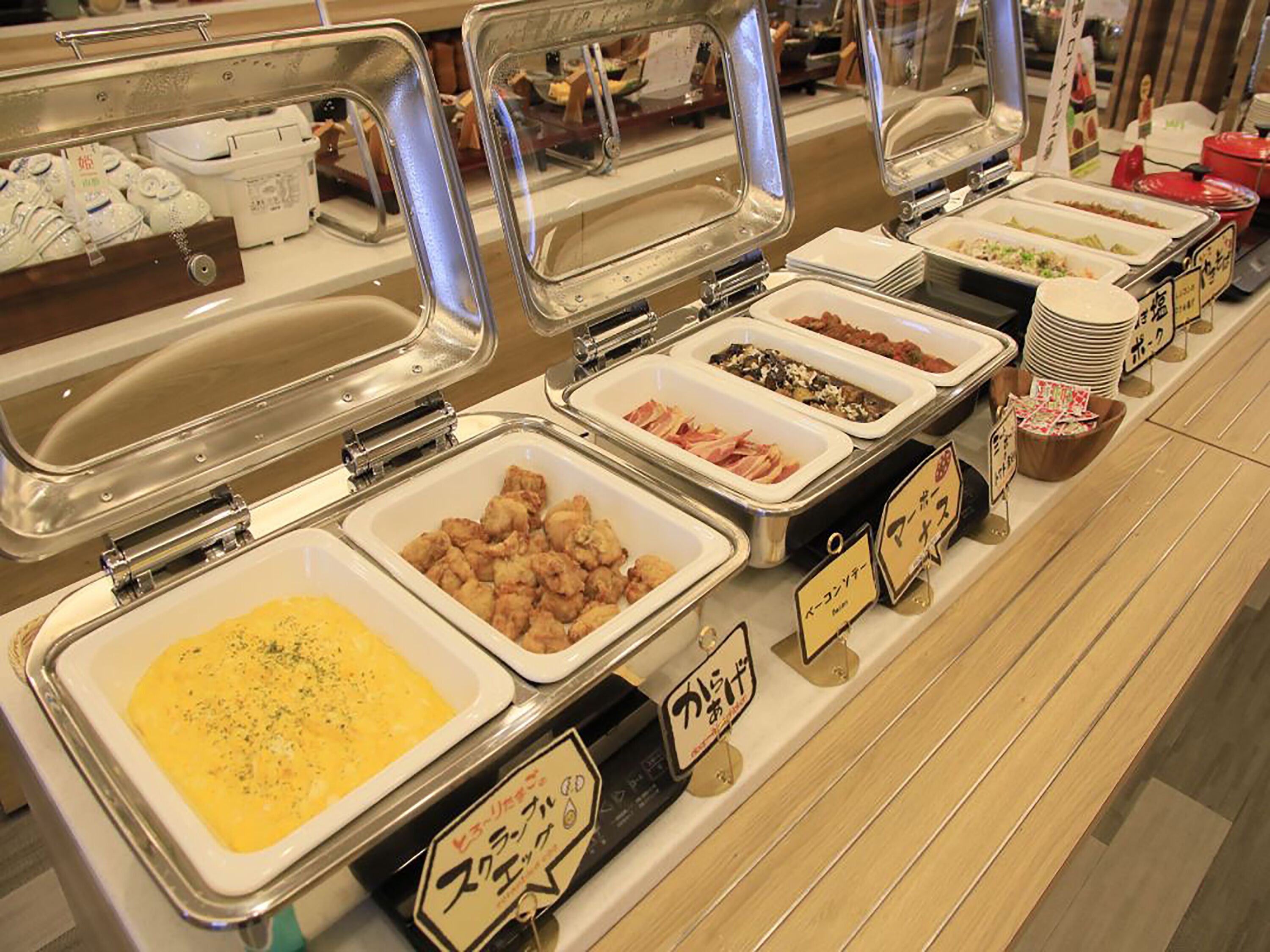 Ein Buffet mit verschiedenen Speisen in separaten Behältern, die jeweils mit Schildern beschriftet sind.