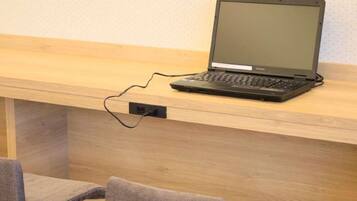 Un ordinateur portable est posé sur un bureau en bois, et un câble le relie à une prise de courant.