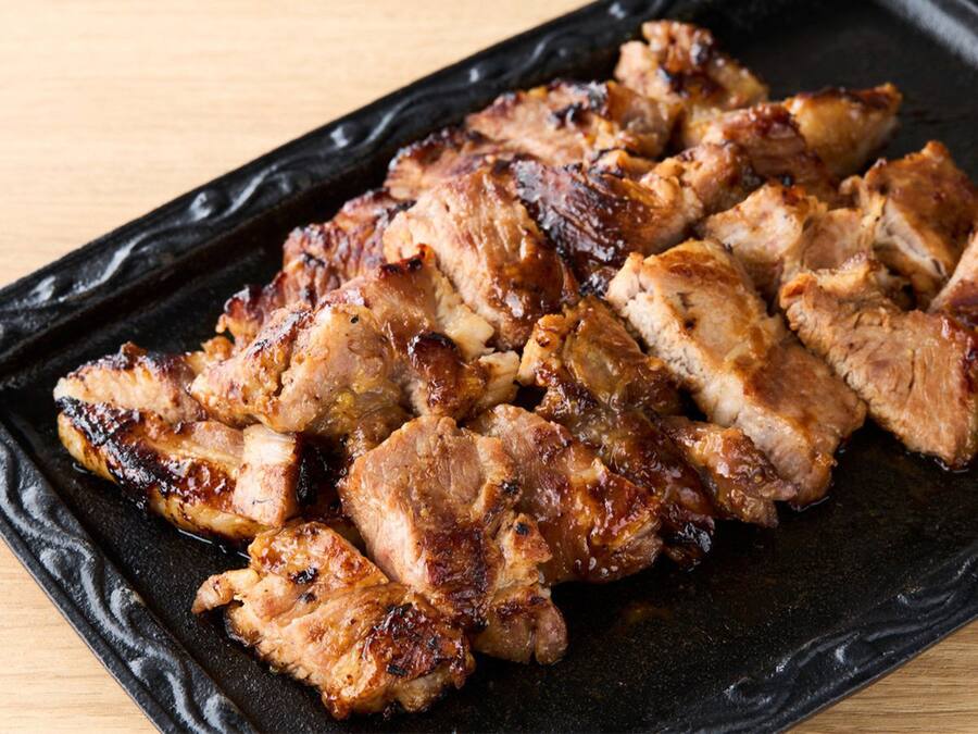 Un plato rectangular negro con tiras de cerdo a la parrilla.