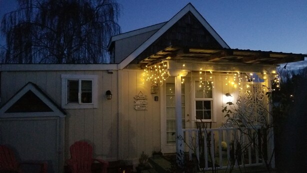 Een klein huis met een veranda, versierd met lichtslingers, een witte deur en een klein raam.