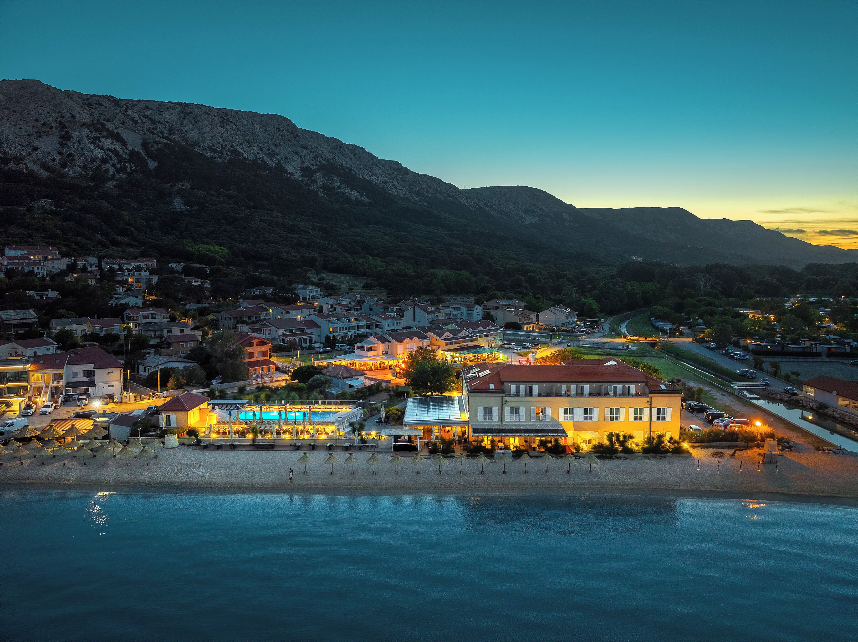 A coastal town with a beach, a pool, and a mountain backdrop.