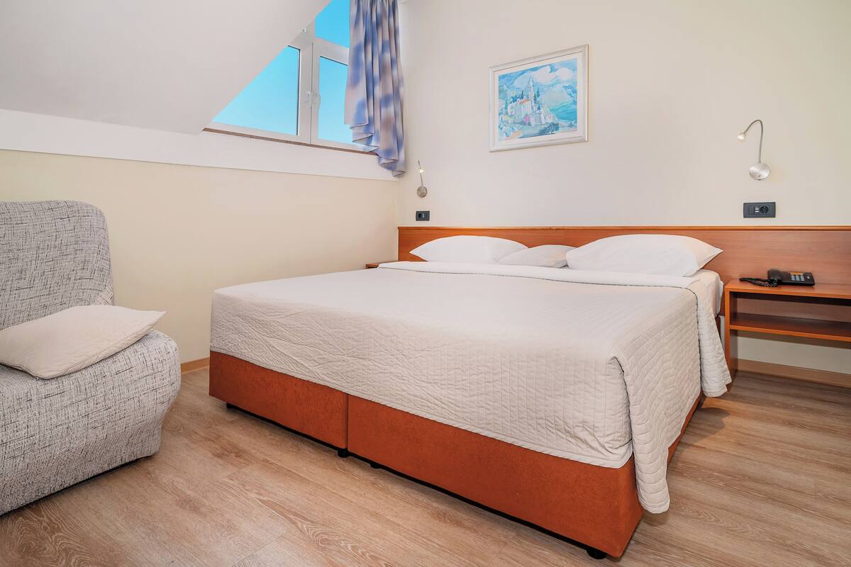 A bedroom with a bed, a chair, a desk, and a painting on the wall.