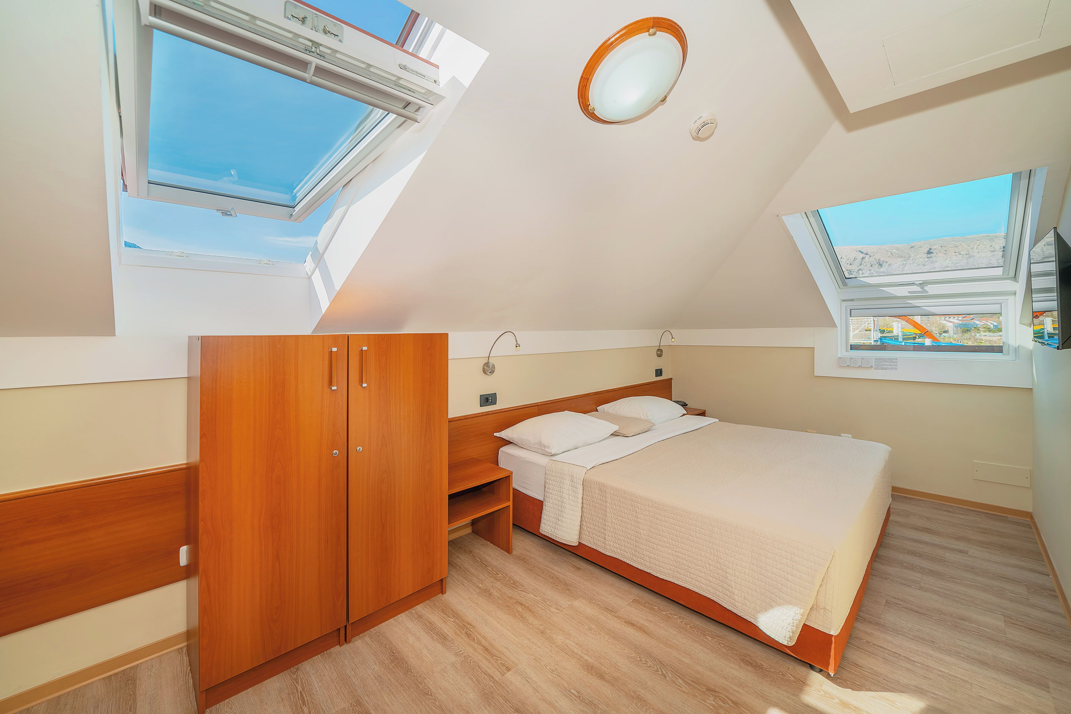 Un dormitorio con tragaluz, cama, armario de madera y un pequeño banco.