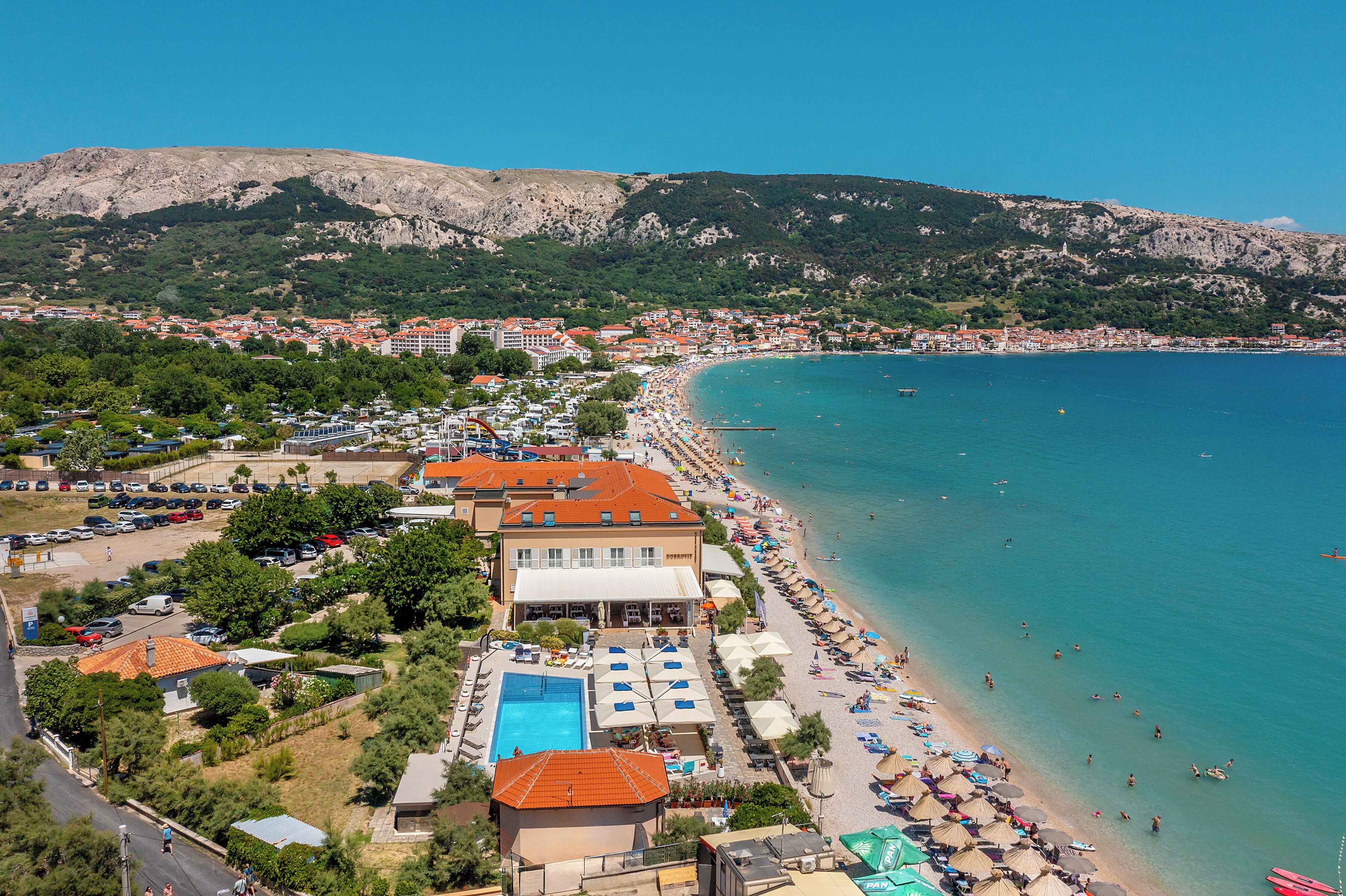 Un hotel sulla costa con piscina, vista sulla spiaggia e montagne sullo sfondo.