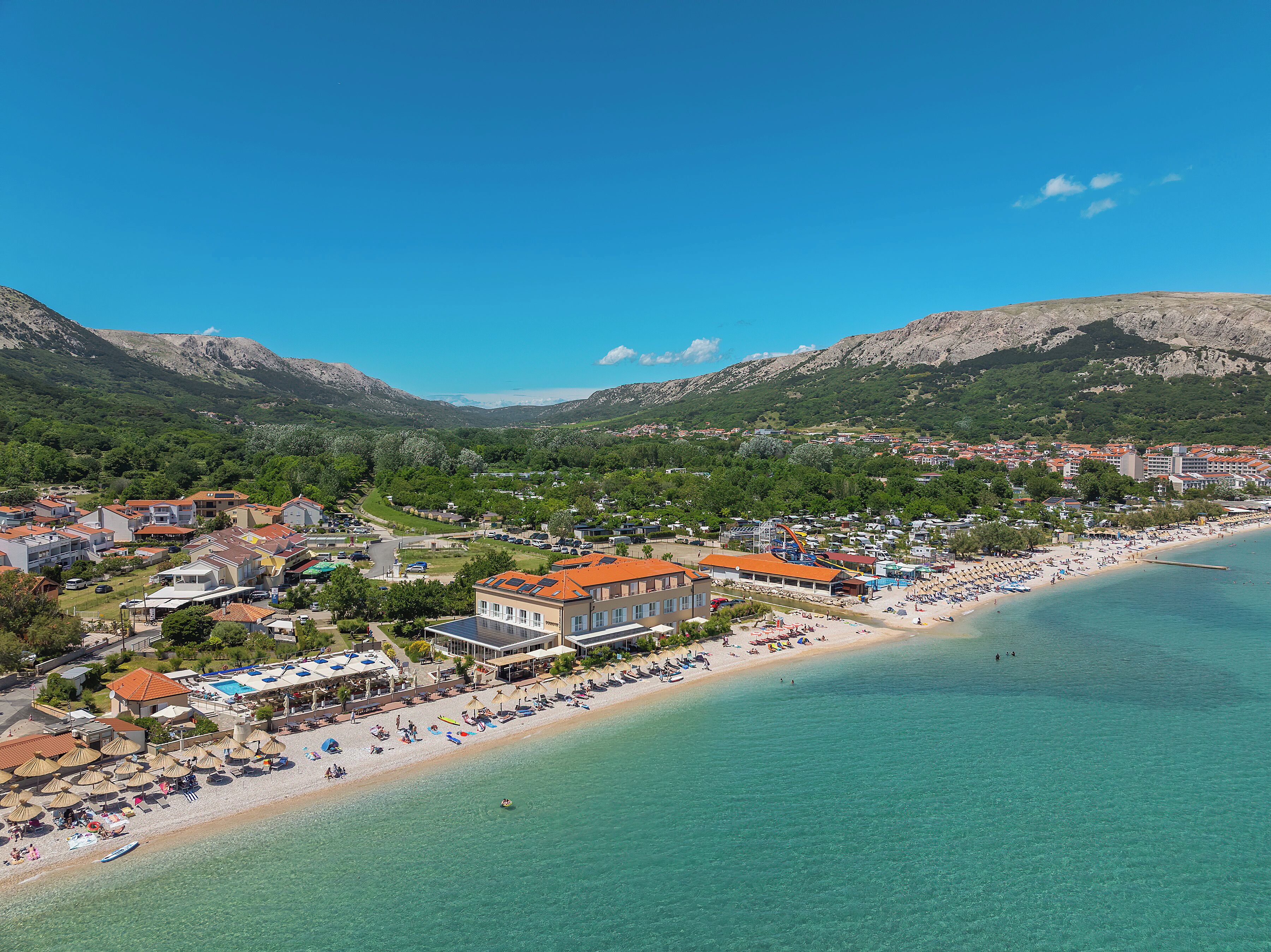 A coastal town with a beach, buildings, and mountains in the background.