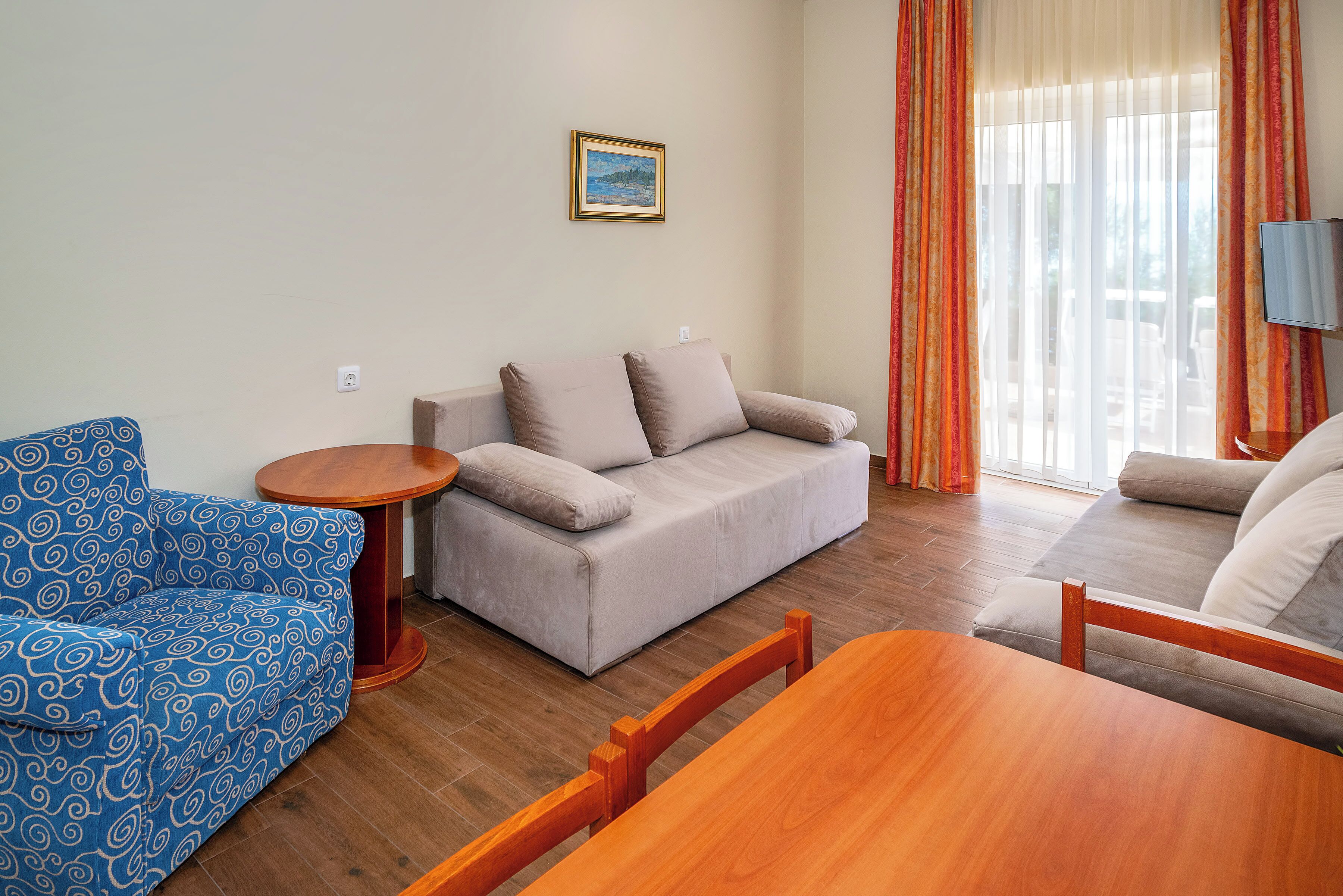 A living room with a sofa, a blue patterned chair, a wooden table, and a television.
