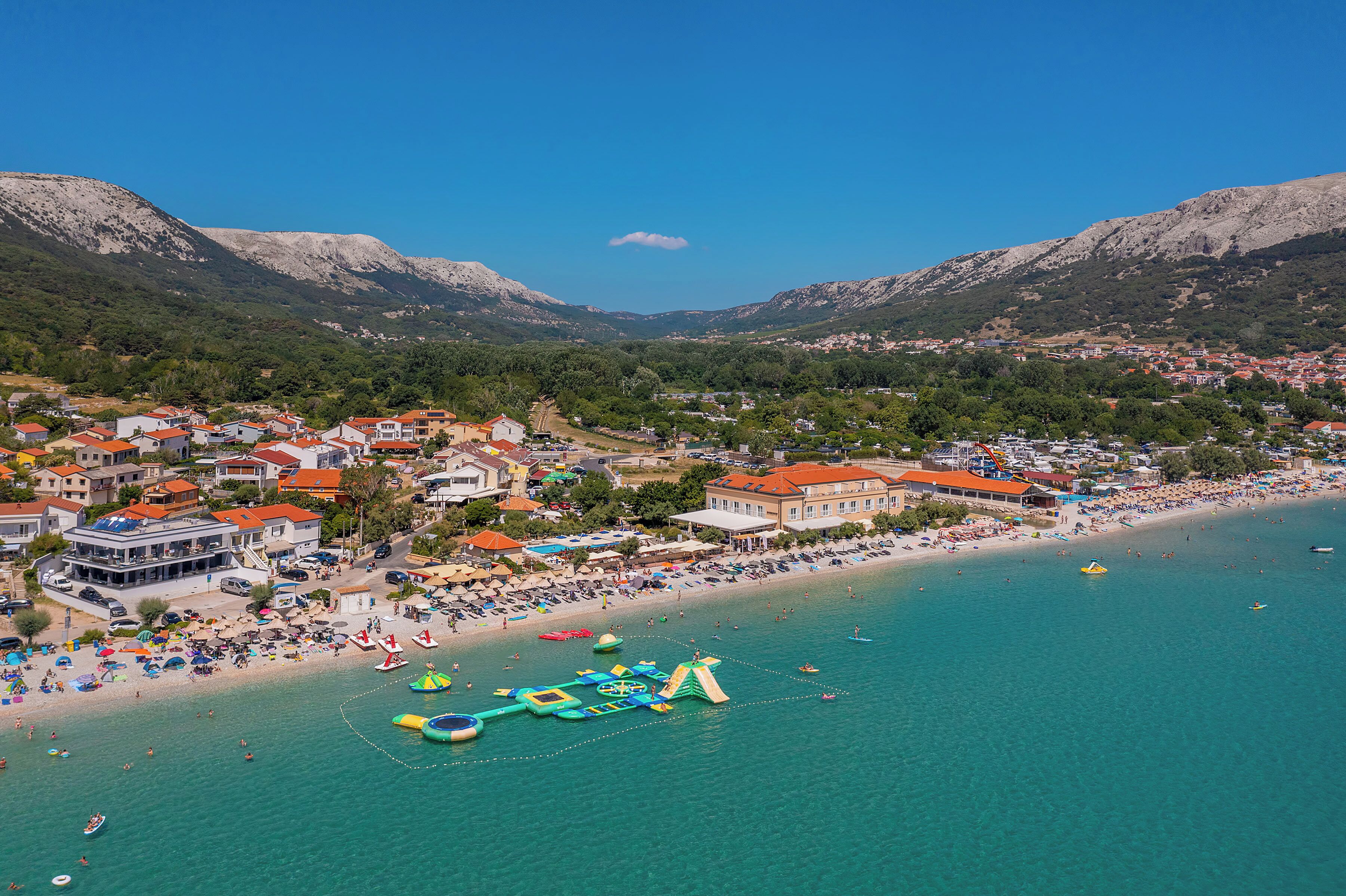 Un pueblo costero con una playa, casas y montañas al fondo.