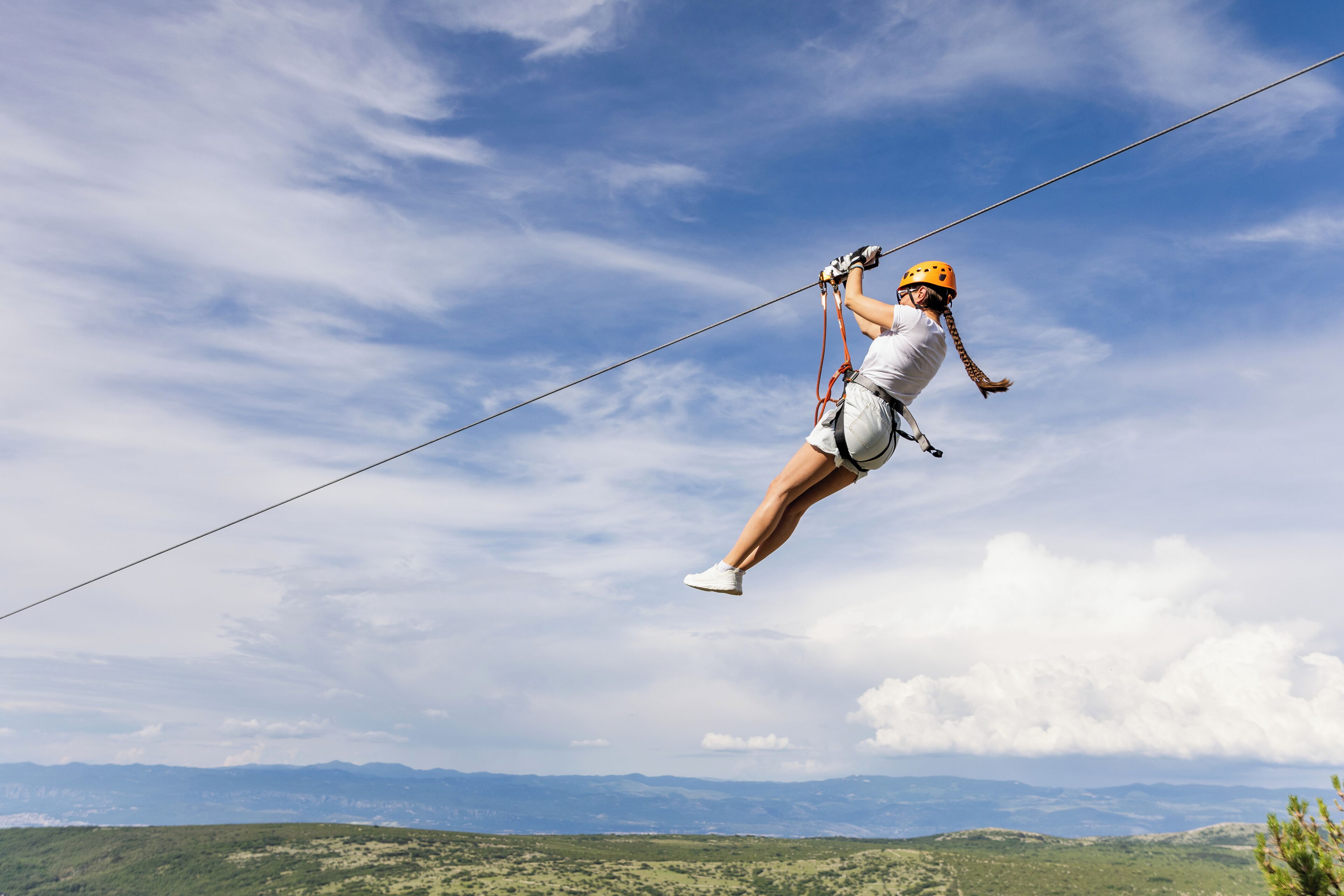 A person zip-lining across a landscape with mountains in the background.