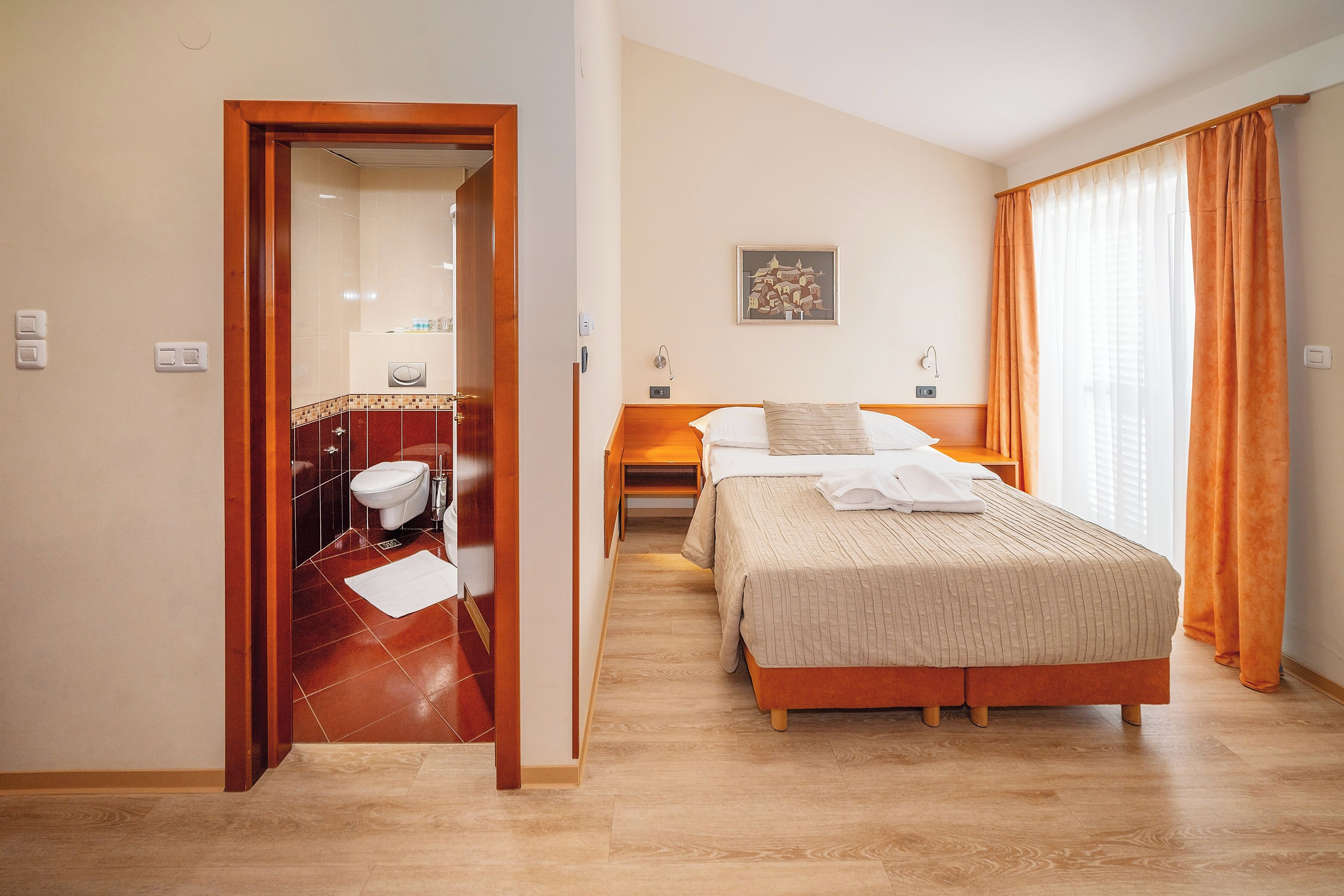 A hotel room with a wooden bed, a bedside table, a nightstand, and a bathroom with a toilet and sink.