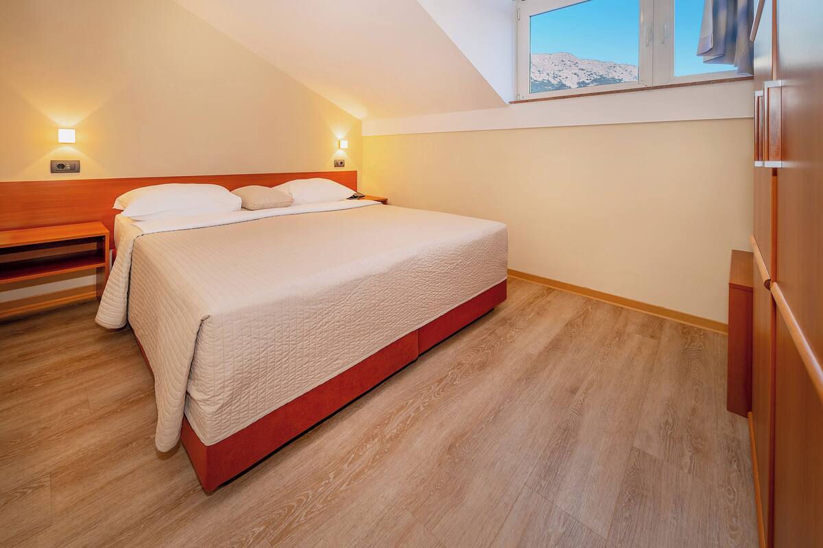 A bedroom with a bed, bedside tables, and a window with a mountain view.