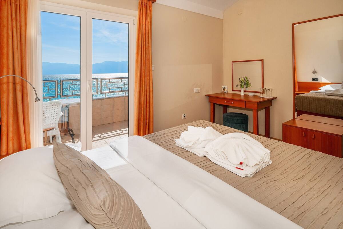 A hotel room with a bed, a desk, a chair, a mirror, and a view of the sea.