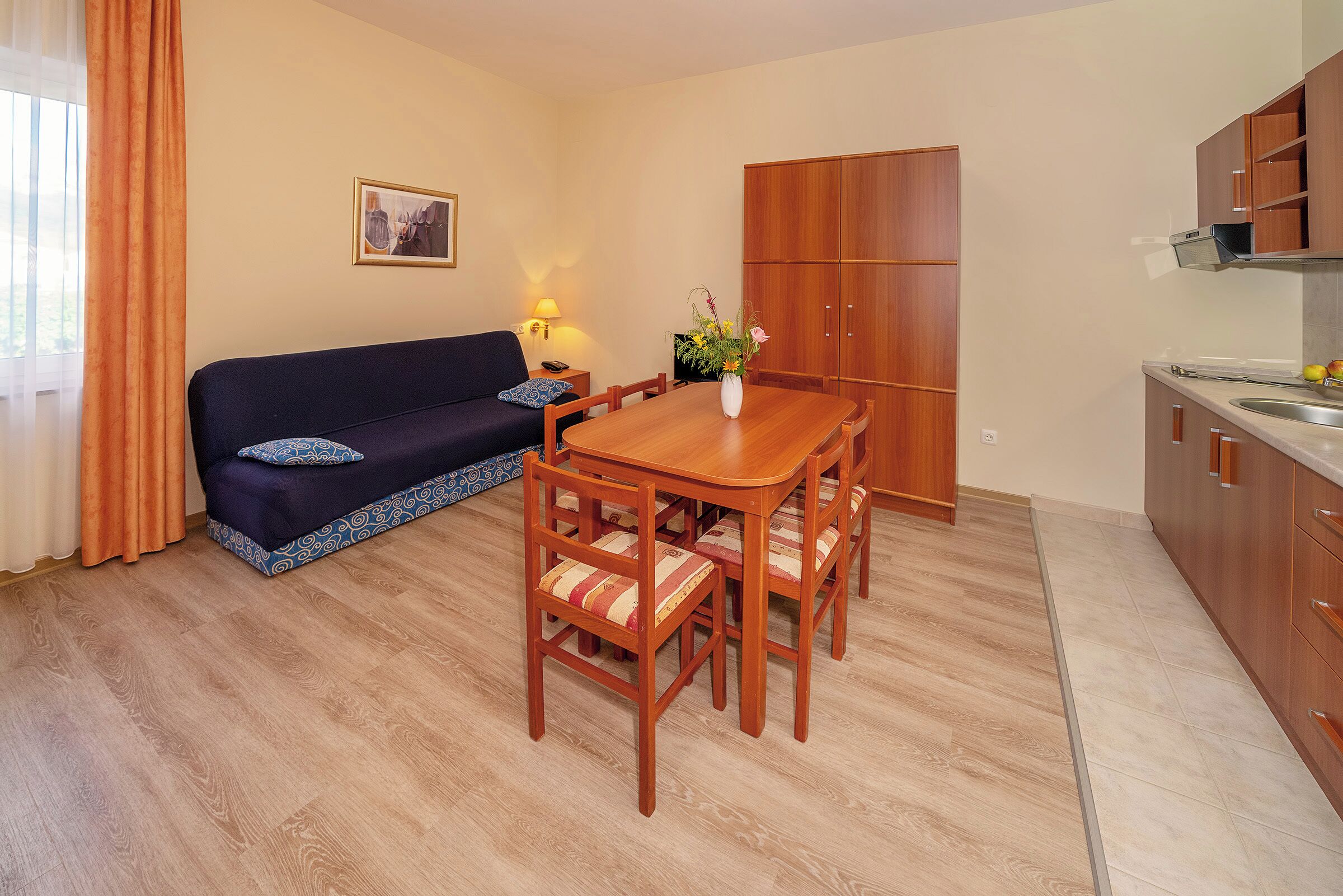 A compact living space with a wooden dining table, matching chairs, a sofa, and a kitchen area.