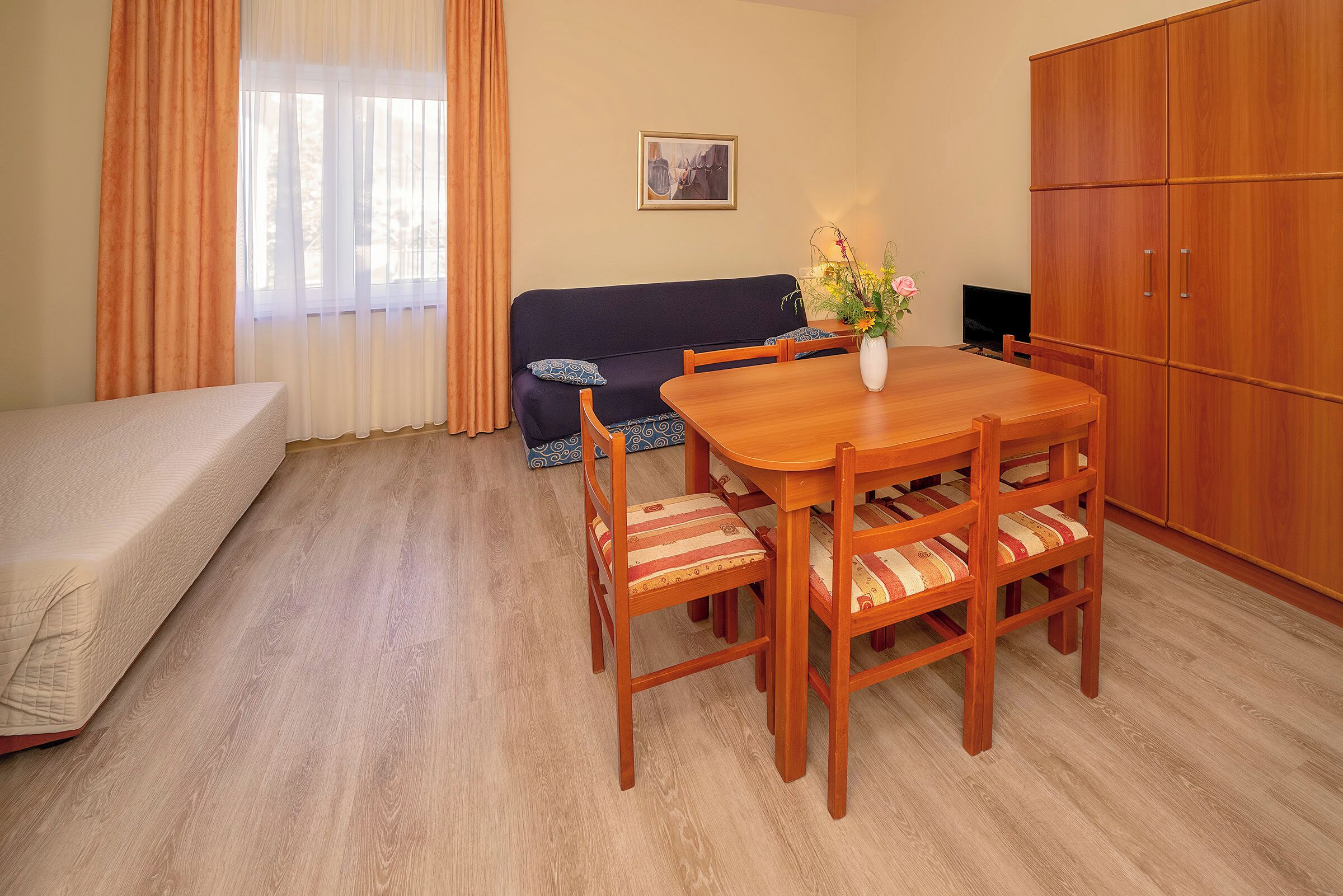 A room with a wooden dining table, four chairs, a sofa, a TV, and a cabinet.