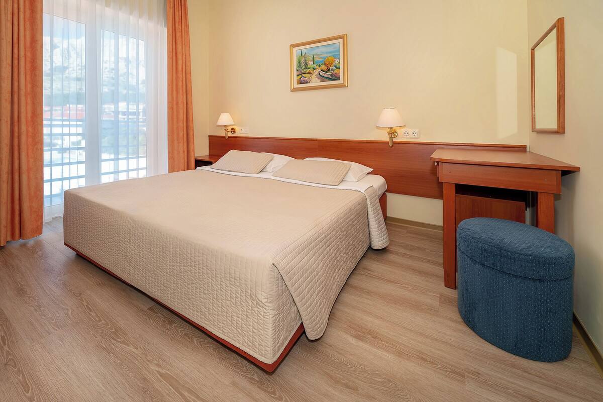 A hotel room with a bed, bedside tables, a desk, a chair, and a window with curtains.