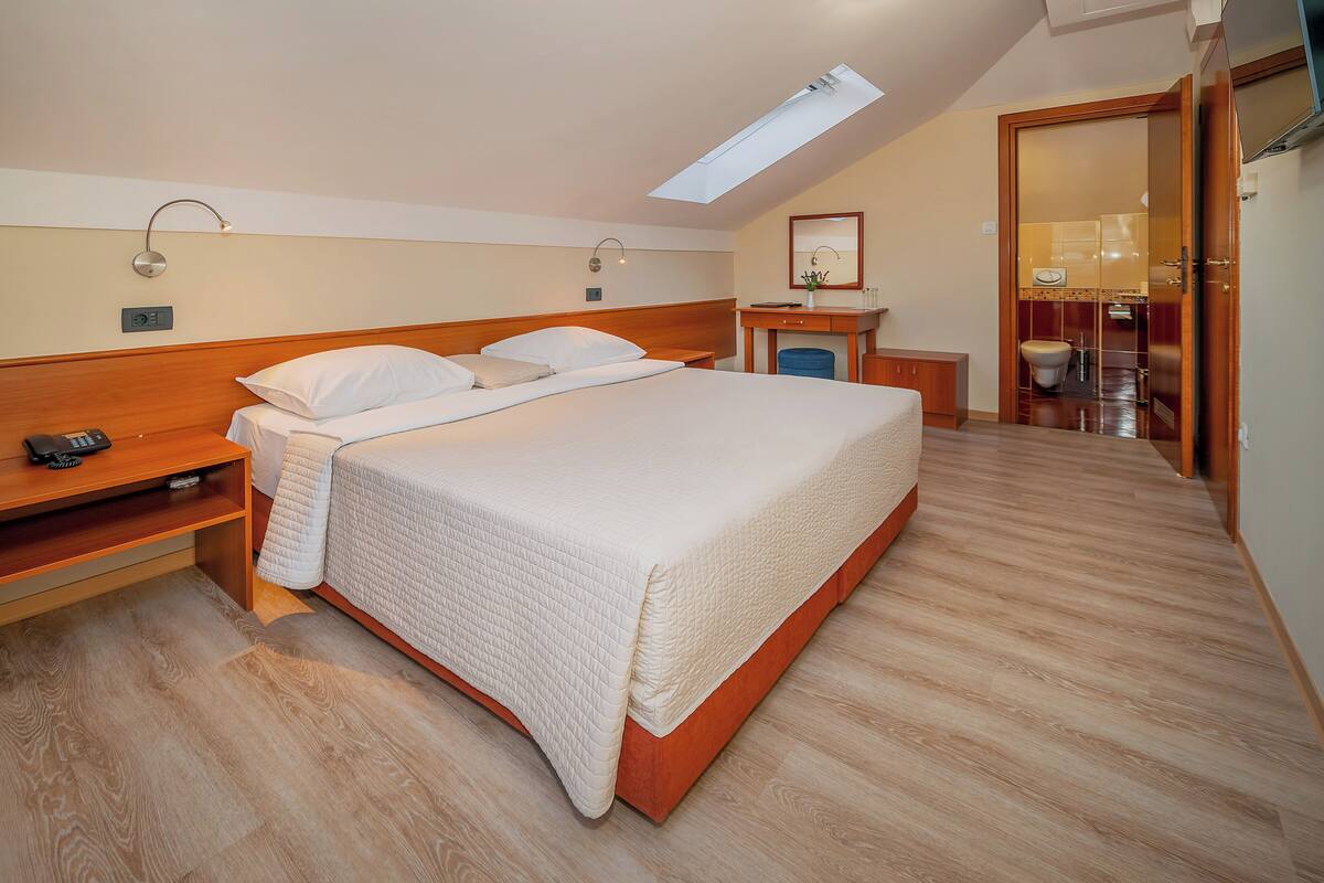 A hotel room with a large bed, bedside tables, a desk, and a bathroom visible through an open door.