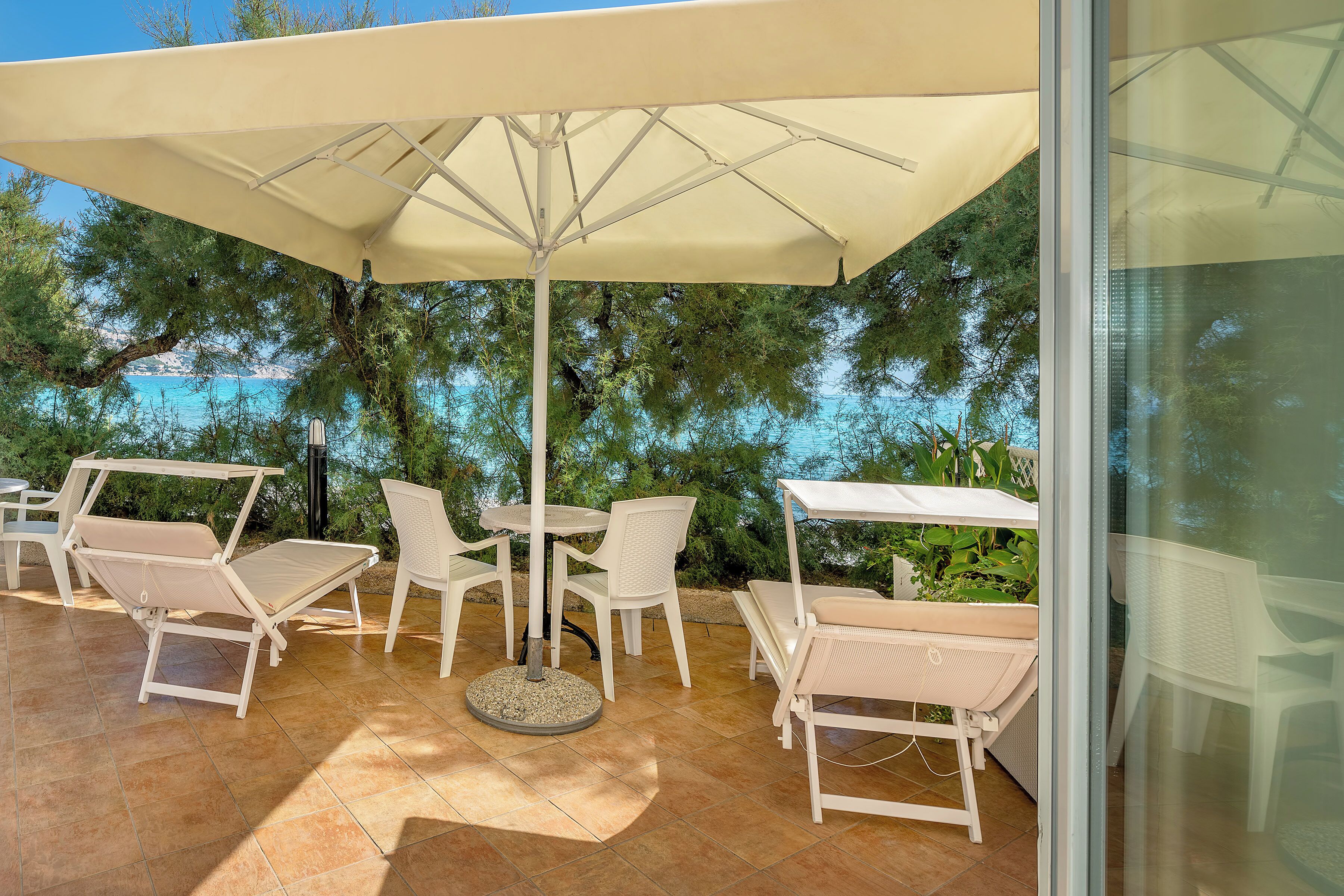 An outdoor patio with white furniture, including chairs and a table, under a large umbrella.