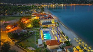 Un hotel junto a la costa con piscina, sombrillas de playa y vistas al mar y a las montañas.