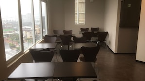 Une salle de conférence équipée de tables et de chaises, de grandes fenêtres donnant sur la ville et une porte menant à une autre pièce.