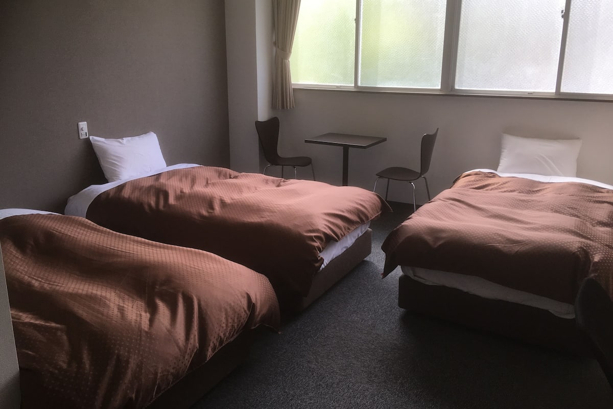 Een hotelkamer met twee bedden, een tafeltje, twee stoelen en een raam met gordijnen.