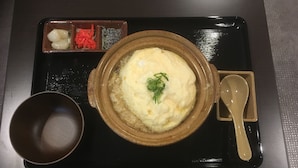 Un bol de riz garni d’herbes vertes, un petit bol de légumes marinés et une cuillère sur un plateau noir.