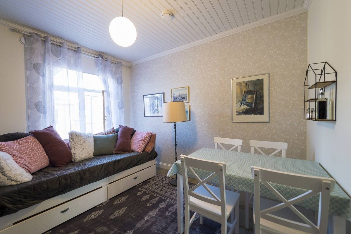 A cozy room with a sofa bed, a dining table with chairs, a lamp, and wall art.