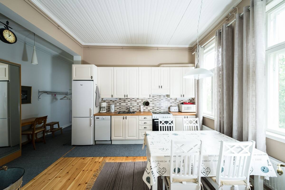 A compact kitchen with white cabinets, a refrigerator, and a dining area with a table and chairs.
