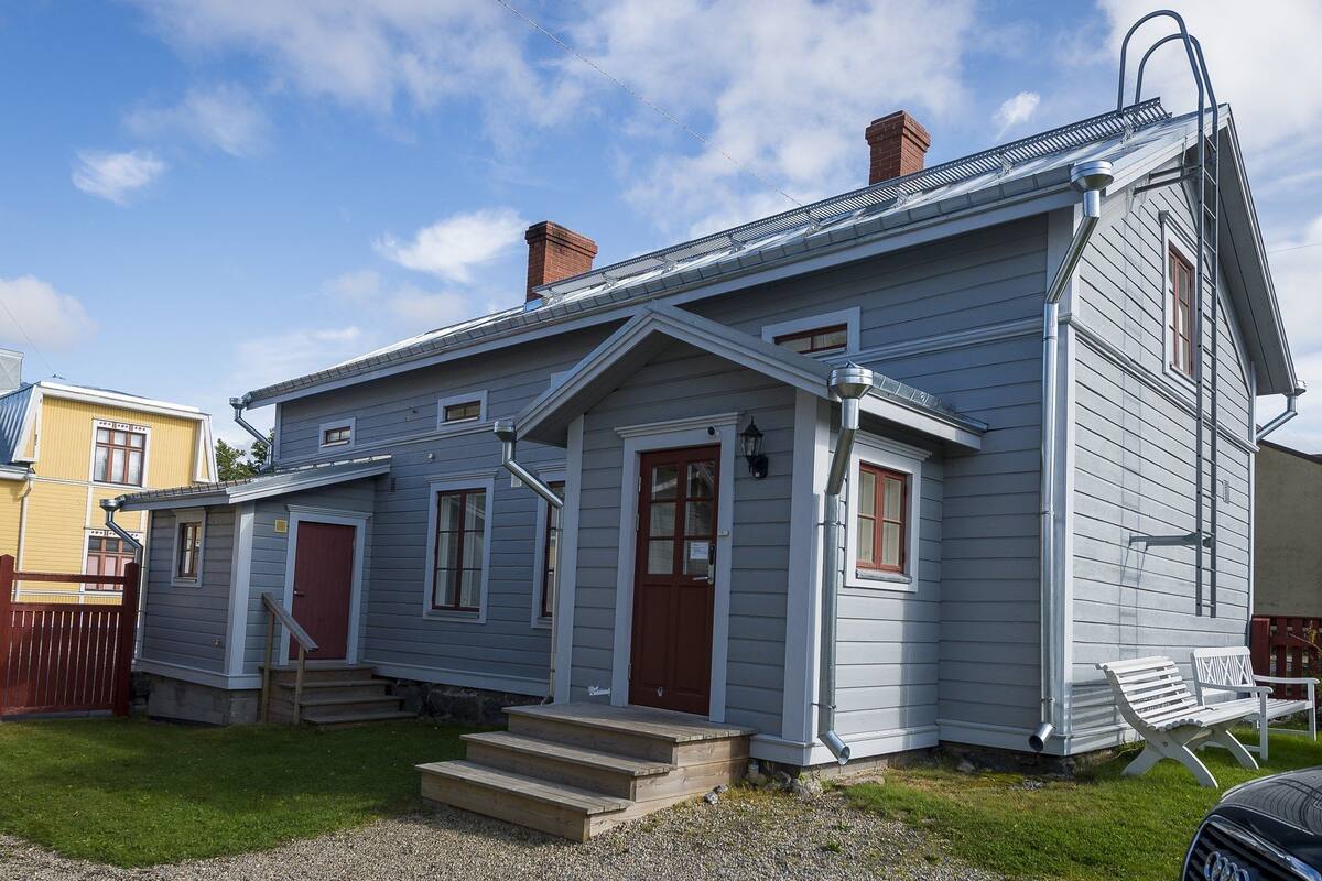 A two-story house with a front porch, a red door, and a white bench outside.