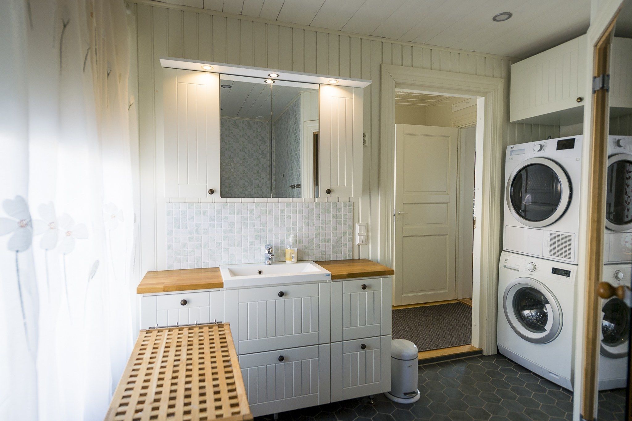 A compact laundry room with a sink, mirror, and stacked washing machines.