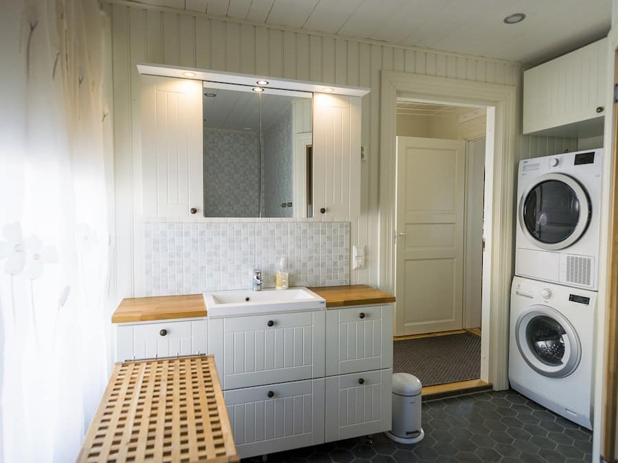 A compact laundry room with a sink, mirror, and stacked washing machines.