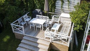Une terrasse en bois, agréée de mobilier d’extérieur, notamment une table et des chaises, et entourée de verdure.