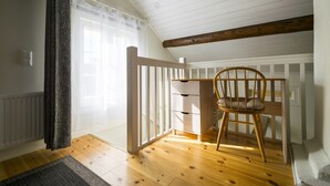 Une pièce avec un plancher en bois, un plafond blanc avec des poutres apparentes, une chaise en bois et une commode blanche.
