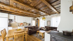 Un salon chaleureux avec une table à manger en bois, deux canapés et un coin cuisine doté de meubles blancs et d’une cuisinière.