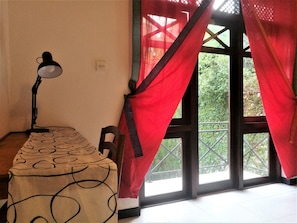 A room with a desk, a lamp, a chair, and a window with red curtains. - Bhakthi Yoga Sri Lanka (Colombo)