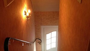 Un escalier en bois avec une rampe, un luminaire fixé au mur et une porte en haut.