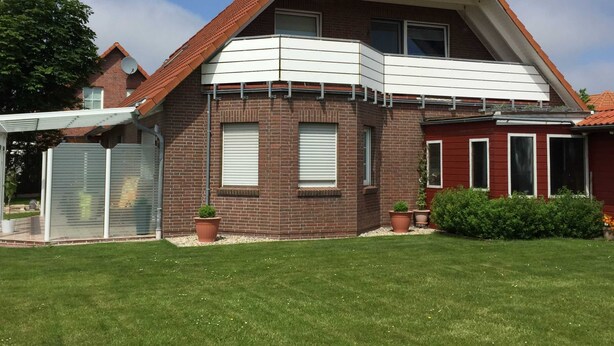 Une maison à deux étages, avec un toit recouvert de tuiles rouges, un balcon et une terrasse couverte.