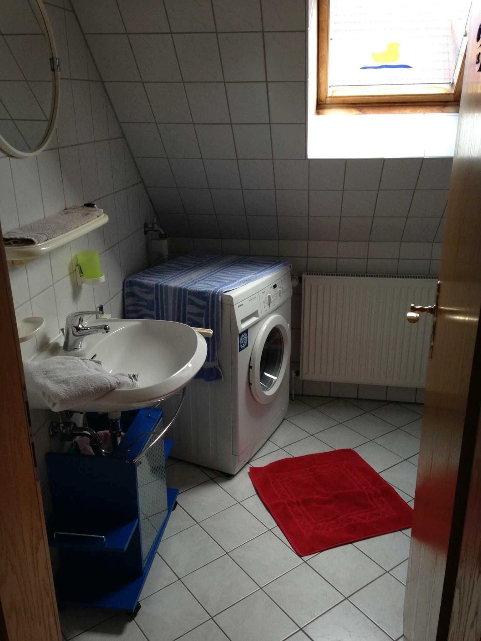 A compact laundry room with a washing machine, a sink, and a small window.