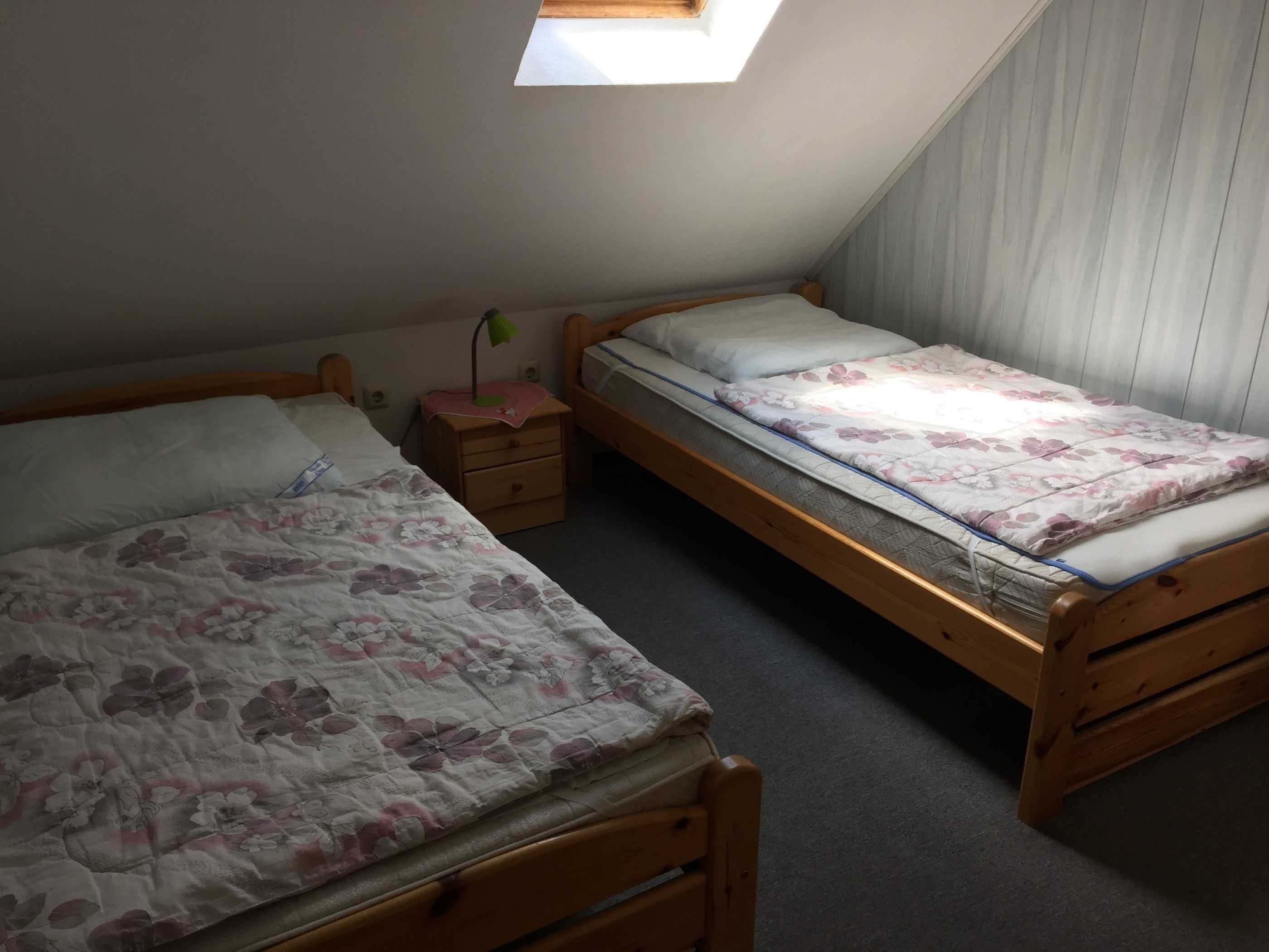 A small, dimly lit room with two wooden beds, a nightstand, and a skylight.