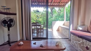 Une pièce avec une table en bois, un ventilateur et une vue sur un patio extérieur doté d’un mur en pierre et d’un banc.
