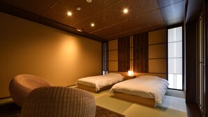 Una habitación tradicional japonesa con suelo de tatami, dos camas, un techo bajo de madera y una puerta corrediza con vistas al exterior.