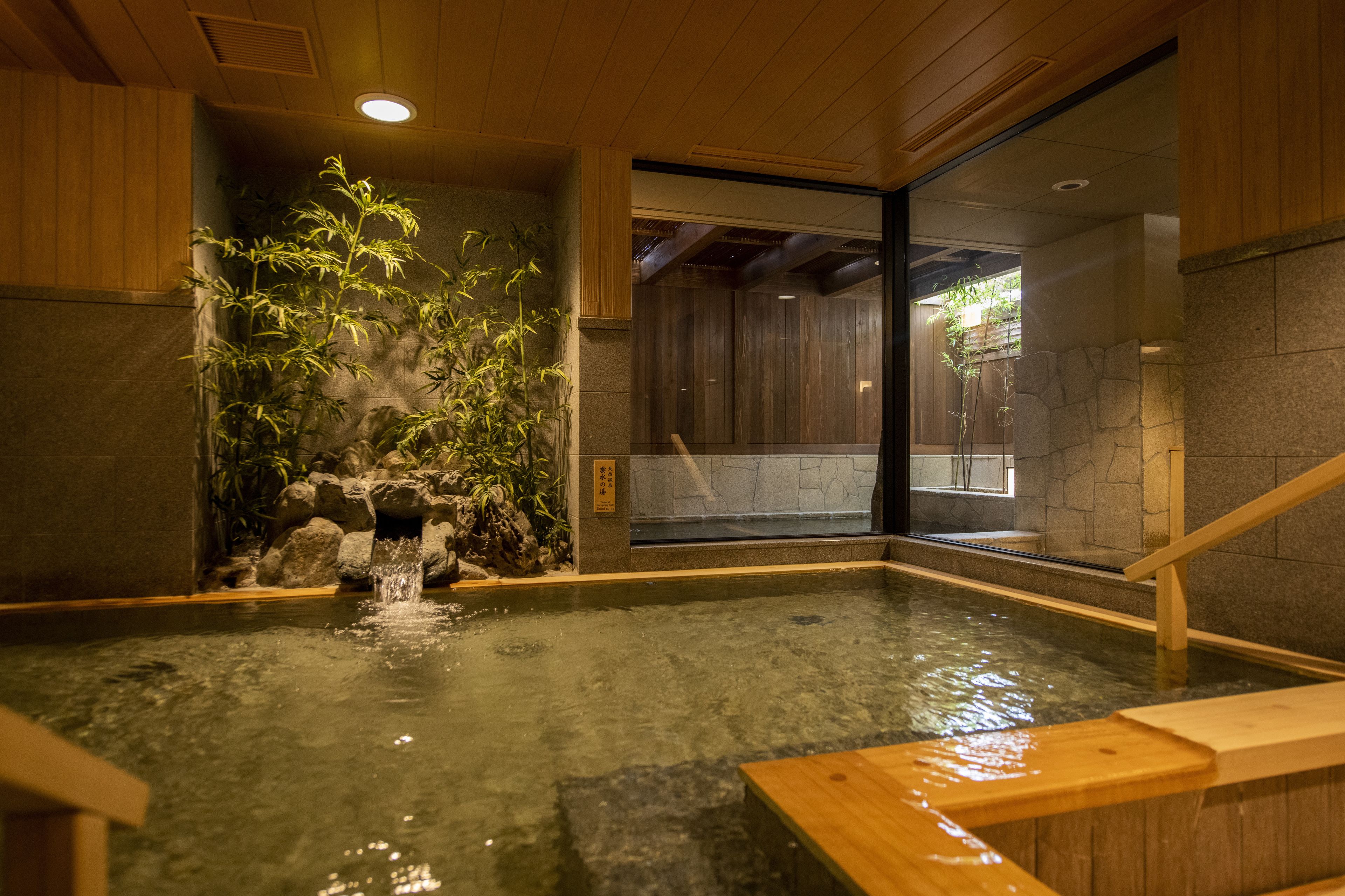 A traditional Japanese onsen with a wooden interior, a stone wall, and a bamboo plant.