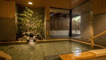 A traditional Japanese onsen with a wooden interior, a stone wall, and a bamboo plant.